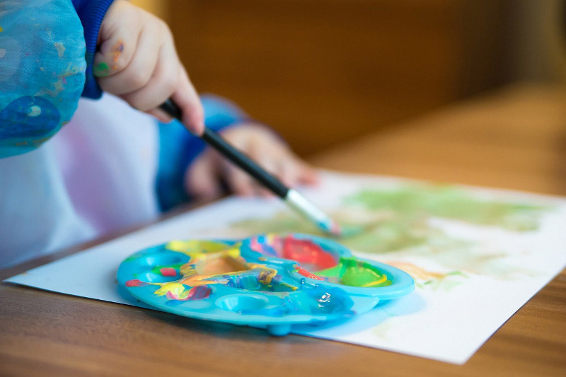 L’immagine mostra la mano di un bambino o di una bambina che colora un disegno
              a tempera